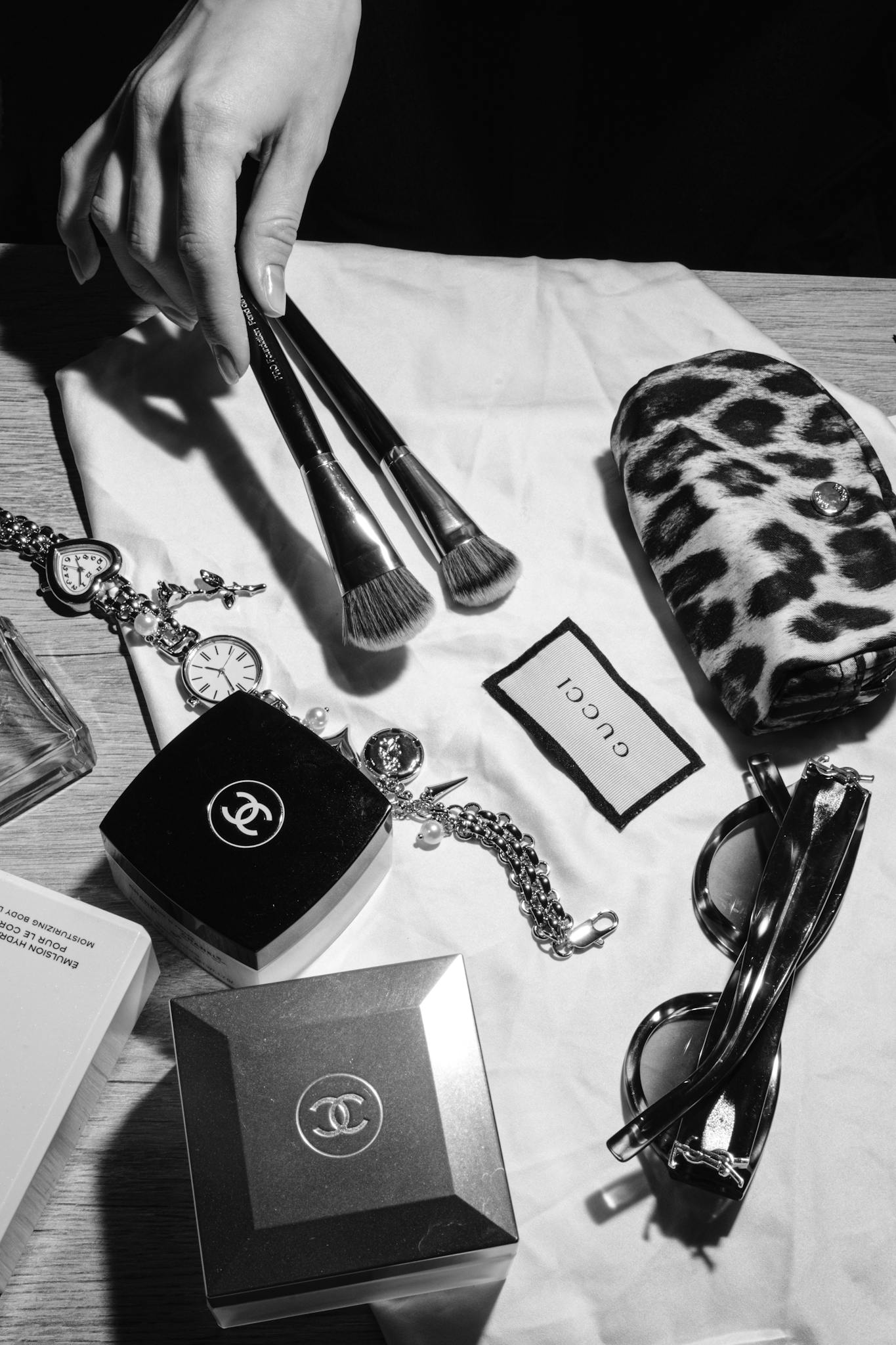 A stylish black and white flat lay of luxury fashion accessories including makeup and jewelry.